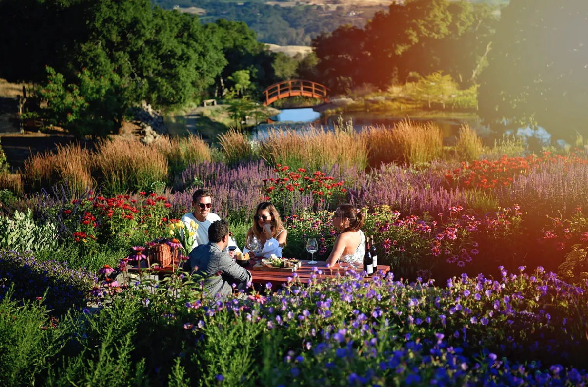 A group of friends enjoying a wine tasting picnic among fields of flowers next to a pond