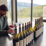 Matt swirling a glass of wine with a lineup of Coursey Graves wine bottles